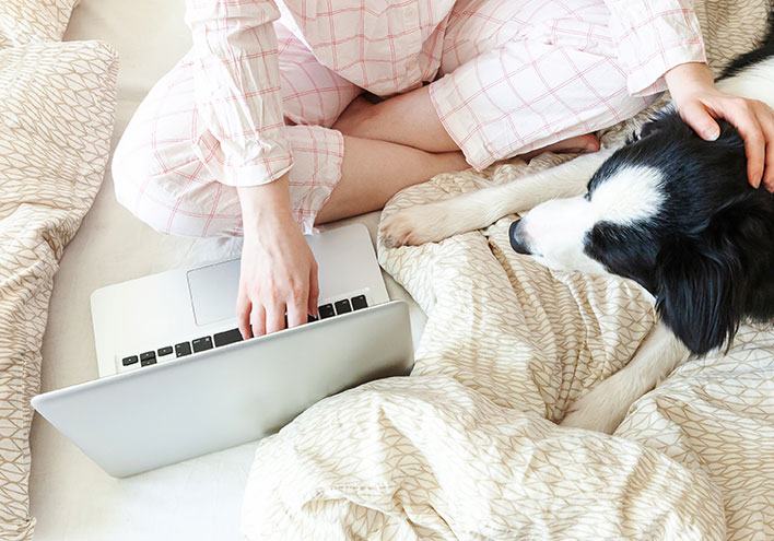 Image of woman using laptop on bed with dog
